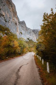 Asphalt road in autumn day. Landscape with beautiful empty mountain road with a perfect asphalt, high rocks, trees and cloudy sky. hipster toning. Travel background. Highway at mountains. Speed