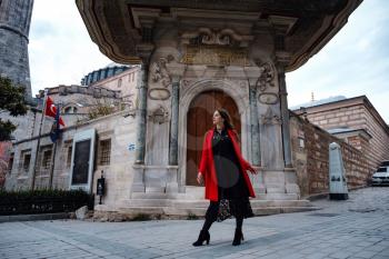 Woman enjoy walk near Hagia Sophia Cathedral, famous islamic Landmark mosque, Travel to Istanbul, Turkey. Latin American woman or Turkish woman in a red stylish coat