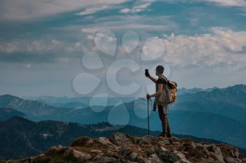 silhouette of Young male hipster in the mountains in autumn take a picture on the smartphone. Discovery Travel Destination Concept. Tourist on the high rocks background. Sport and active life concept.