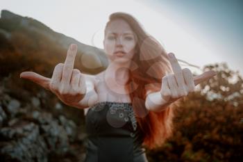 beautiful furious scandinavian warrior ginger woman in grey dress with metal chain mail. woman showing middle finger - gesture of fuck, expression, provocation and rude attitude.