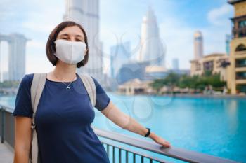 Portrait of beautiful woman wearing a mask for prevent virus walking in Dubai with skyscrapers in the background. Enjoying travel in United Arabian Emirates. Waiting for the evening fountain show