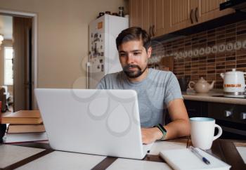 young man freelancer using laptop studying online or working from home, happy casual millennial guy typing on pc notebook surfing internet looking at screen enjoying distant job sit at table