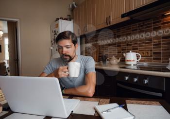 Portrait of happy man having a cup of coffee in kitchen. The guy works from home.