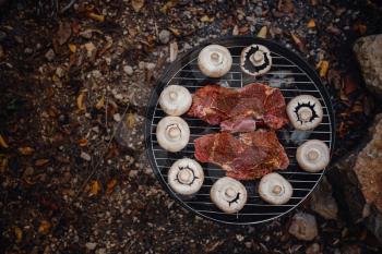 Beef steaks on grill outdoor near river. beef and mushrooms in a portable barbecue outdoors