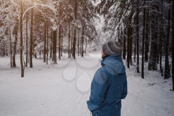 A man breathes deeply in the calm winter forest on a cold day. back view