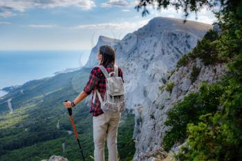 Fit female hiker with backpack and poles standing on a rocky mountain ridge looking out and peaks in a healthy outdoors lifestyle concept