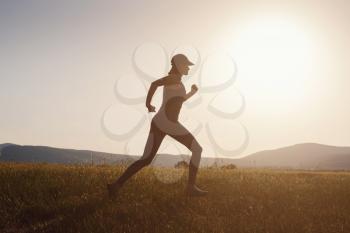 Jogging woman running in summer field at sunset. woman fitness silhouette sunrise jogging workout wellness concept.