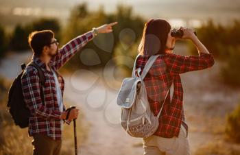 Portrait of happy young couple having fun on their hiking trip. Caucasian and asian hiker couple enjoying themselves on summer vacation. They are watching nature with binoculars.