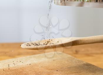 Superfood known as black chia seeds are poured into a wooden backing spoon over wood bread board on kitchen table