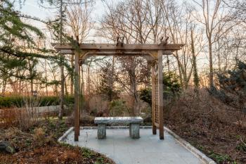 Polished granite seat under a wooden arbor or gazebo in woods at sunset in winter