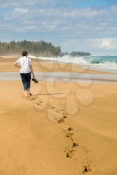 Senior caucasian woman walks down sandy Lumahai beach on Kauai Hawaii