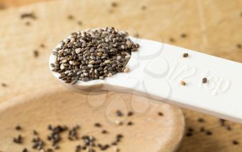 Superfood known as black chia seeds in white plastic measuring spoon over wood bread board on kitchen table