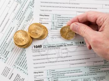 Caucasian hand counting solid gold eagle coins on USA tax form 1040 for year 2014 illustrating payment of taxes to the IRS