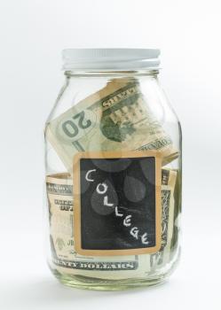 Glass jar on white background with black chalk label or panel and used for saving of US dollar bills for college or educational fees and expenses