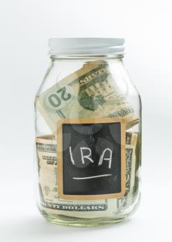 Glass jar on white background with black chalk label or panel and used for saving of US dollar bills for IRA and retirement