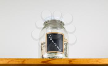 Single glass jar with chalk labels used for saving US dollar bills and notes for college educational fees