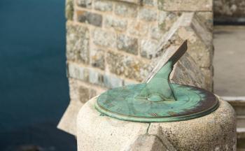Green stained copper or brass sundial fixed to stone wall of castle overlooking the ocean far below