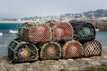 Rope and wooden frame lobster pot or trap stacked on stone wall of harbor on south coast of England