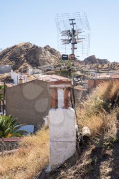 Chimney and TV aerial above cave house built into the hillside of small hill in Purullena near Guadix, Andalucia, Spain