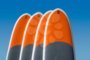Row of four upright standup paddle boards or body boards, surf boards against deep blue sky