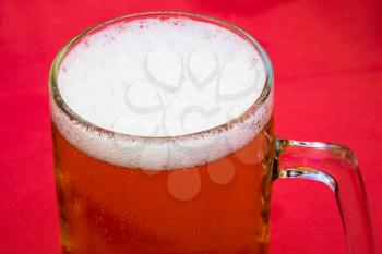 Golden beer, ale or lager in a traditional tankard or mug against red tablecloth background