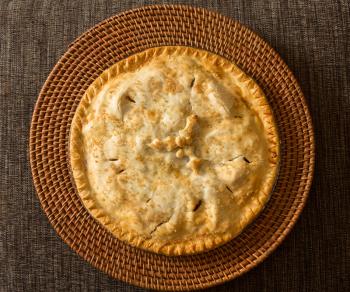 Freshly baked hot apple pie with holly leaves and berries for Christmas or xmas dinner on woven place mat
