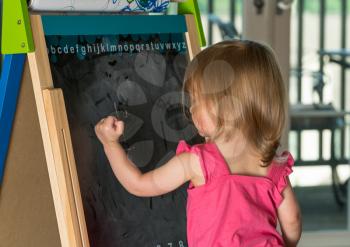 Young two year old girl drawing with chalk on blackboard on an easel during playtime