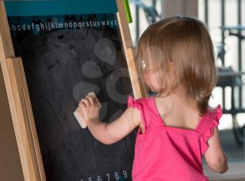 Young two year old girl cleaning a blackboard on an easel during playtime