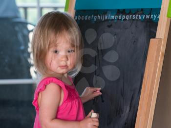 Young two year old girl drawing with chalk on blackboard and studying her subject
