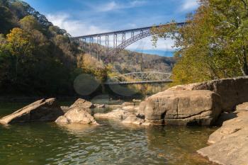 Kayakers float towards the rapids under the high arched New River Gorge bridge in West Virginia