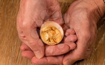 Senior man's hand holding a selection of pure gold USA treasury coins in broken egg shell illustrating financial security of a retirement nest egg