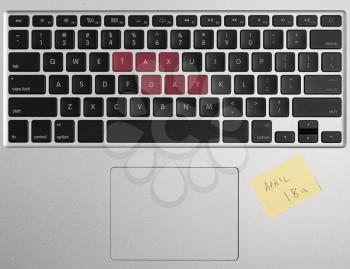 Laptop computer keyboard spelling out April 18 2017 as Tax Day with yellow sticky note as a reminder