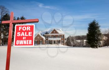 For Sale by owner real estate sign in front of large brick single family house in expansive snow covered yard in mid winter