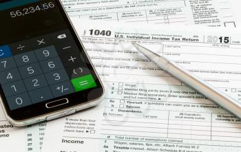 USA tax form 1040 for year 2015 with a pen and calculator app on smartphone illustrating completion of tax forms for the IRS