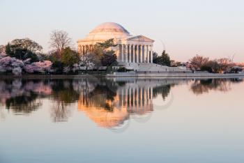 Sun rising illuminates the Jefferson Memorial and Tidal Basin with calm water of Tidal Basin reflecting the monument