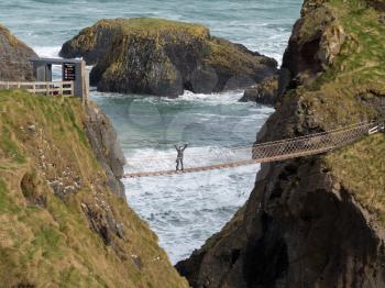Young woman halfway across the Carrick a Rede rope suspension bridge to Carrick Island in Ulster or Northern Ireland County Antrim