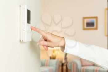 Caucasian female hand pressing button on a modern electronic thermostat timer on wall of a modern home with focus on the screen and fingers of the woman