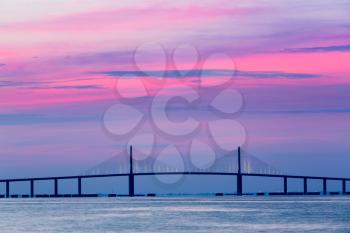 Brilliant sunrise lights up the sky behind Sunshine Skyway Bridge from St Petersburg Florida across Tampa Bay.