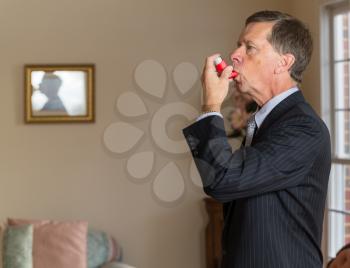 Senior caucasian man  in suit at home with asthma inhaler to handle problems with breathing