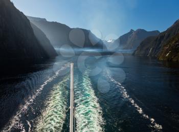 Passengers on cruise ship sailing out of Milford Sound on South Island of New Zealand in early morning. Smog and pollution from the ship float in the valley