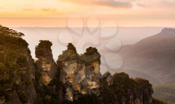Rising sun illuminates the Three Sisters rock formation in the valley from Echo Point overlooking the majestic Blue Mountains near Sydney NSW Australia