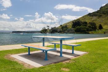 Bay and harbour at Tauranga with picnic table on the sandy beach by calm water in front of the Mount