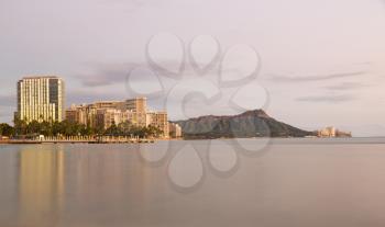 Panorama of the skyline of Waikiki at sunset or dusk taken with a long exposure to blur out movement in the water and provide a reflection of Diamond Head in Hawaii