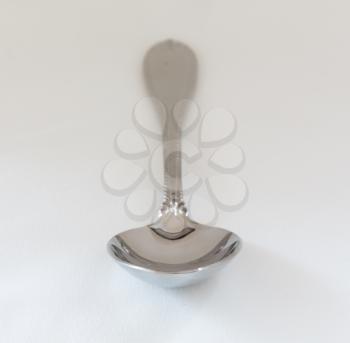 Decorated serving or dessert spoon in front view on fine white tablecloth with pattern just visible