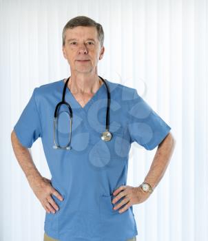 Senior male caucasian doctor with stethoscope in medical scrubs and confidently facing the camera in portrait