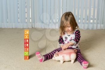 Young girl on floor of home saving money in a piggy bank for college educational expenses in the future