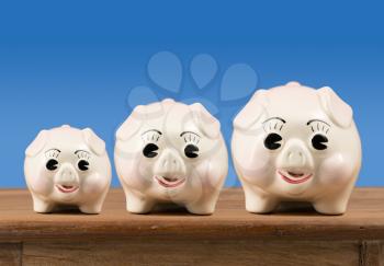Three piggybanks in small, medium and large sizes sitting on a wooden shelf or table waiting for savings