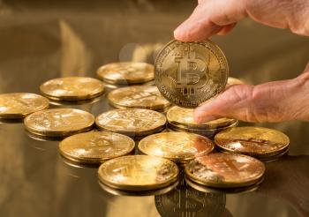 Stack of bit coins or bitcoin on gold background with a single coin held in hand to illustrate blockchain and cyber currency