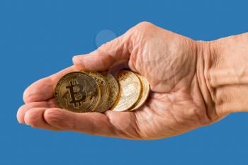 Isolated stack of bit coins or bitcoin held in man's hand on blue background to illustrate blockchain and cyber currency