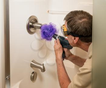 Senior working man cleaning a shower or bath with a power drill